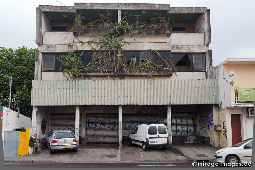 St. Denis
Schlüsselwörter: urban, städtisch, Gebäude, desolat, Pflanzen, Wohnhaus, arm,  grau, Autos, Parkplatz, Beton, heruntergekommen, verwittert, Architektur, ungepflegt, verwildert, Vukaninsel, Insel, urbanlife1, multikulturell, 